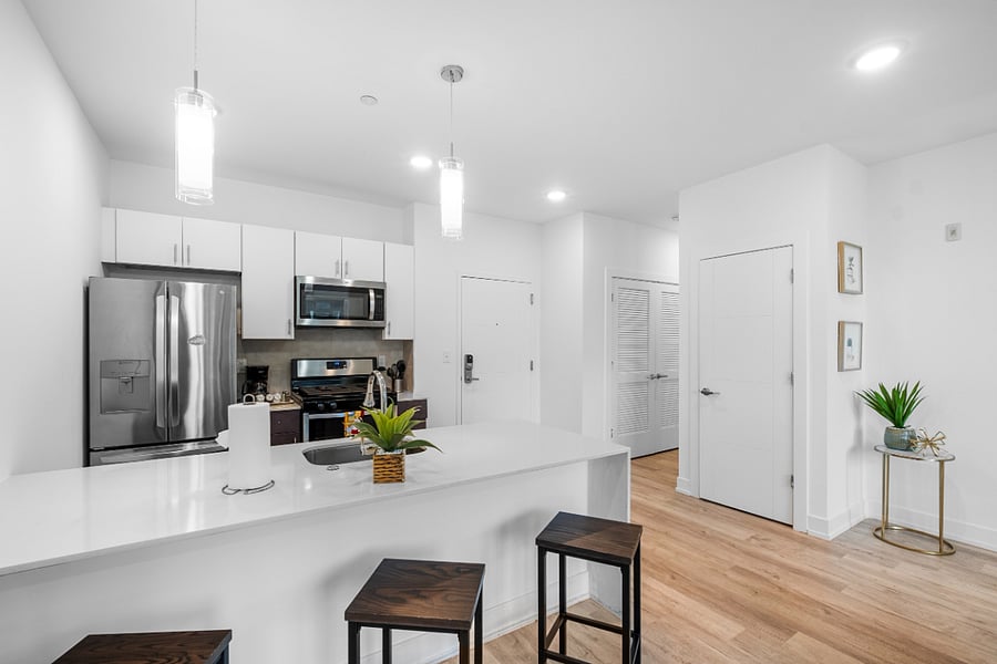 A sleek, modern kitchen with a white quartz island featuring a built-in sink and two elegant blue quilted bar stools. 