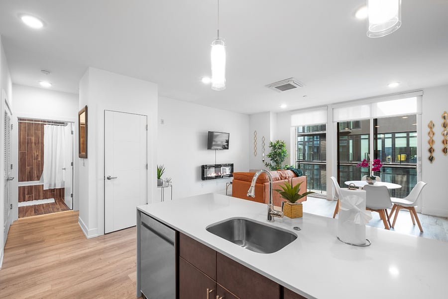 Contemporary open-concept apartment featuring a sleek kitchen island with built-in sink, stainless steel appliances, and dark cabinetry. 
