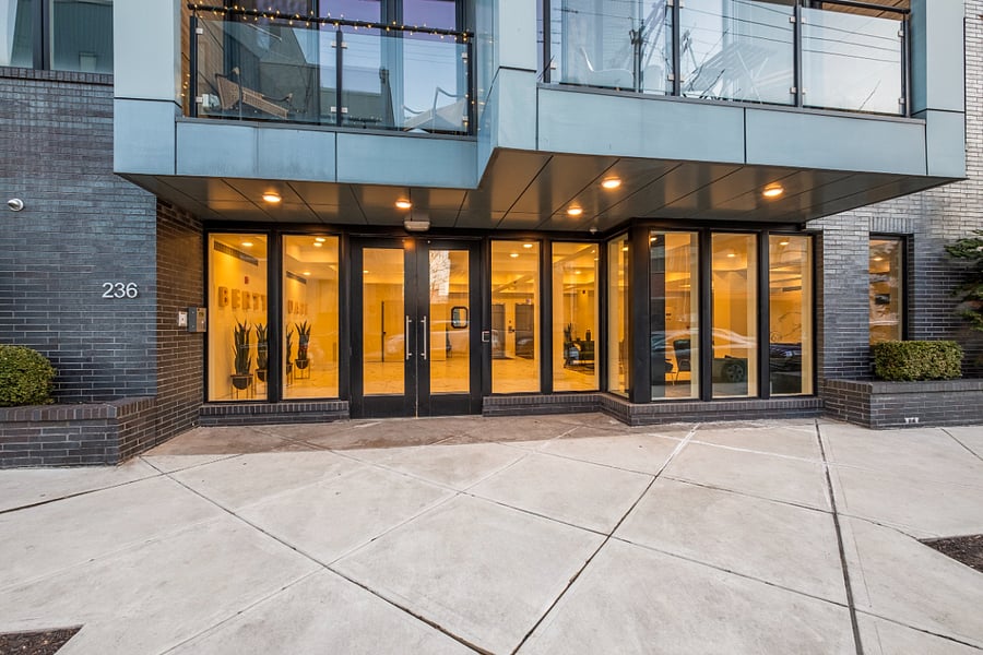 Sleek entrance of a modern building with a striking glass facade. Multiple glass doors and large panels reveal a bright, inviting interior