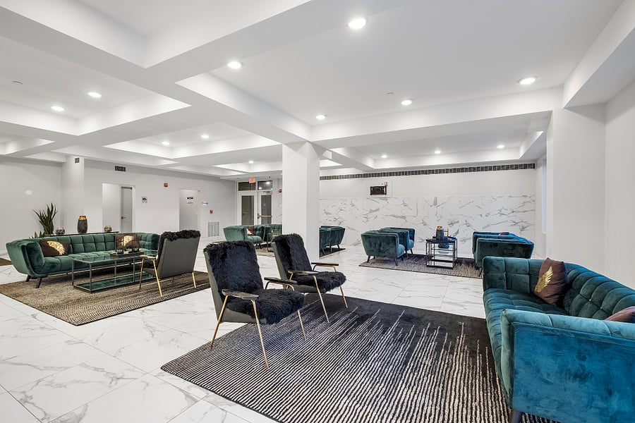 luxurious and spacious lounge area with a modern, minimalist design. Features white marble flooring with gray veining, recessed lighting in a geometric ceiling, and elegant seating arrangements