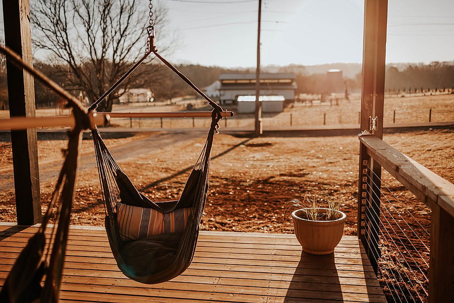 Hanging chairs on front porch with view of farm. 