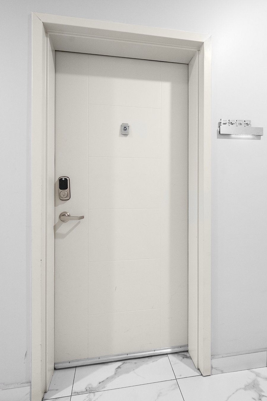 Sleek, modern white door set in a minimalist white wall. The door is equipped with a digital keypad lock and a peephole, emphasizing security and convenience. 