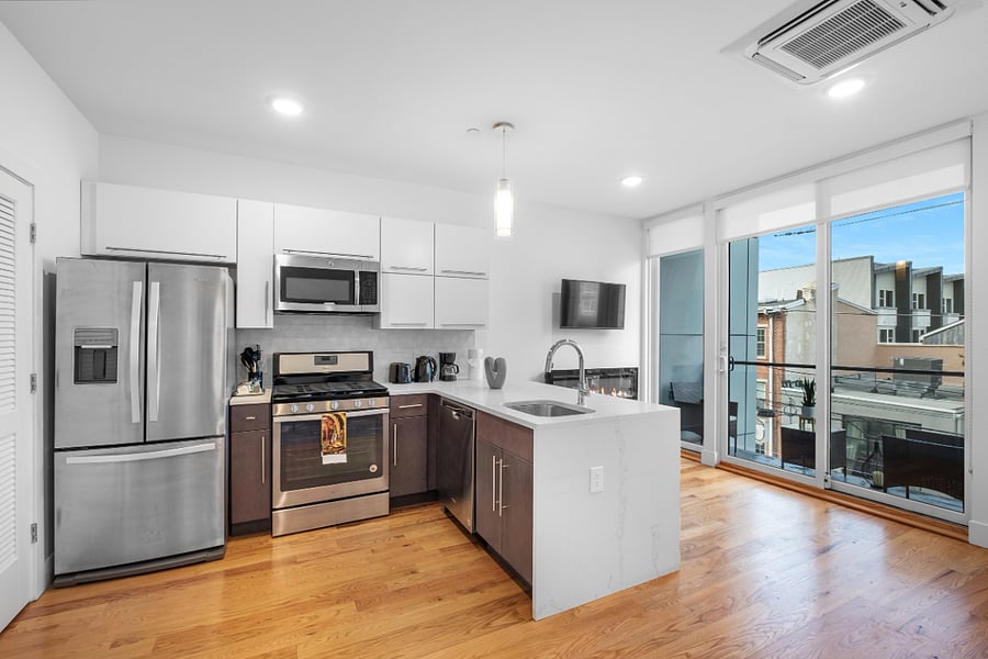 Bright, modern kitchen and living area with sleek stainless steel appliances, a stylish island with a marble countertop, and large windows that flood the space with natural light. The clean design and warm hardwood floors create a cozy yet contemporary vibe.