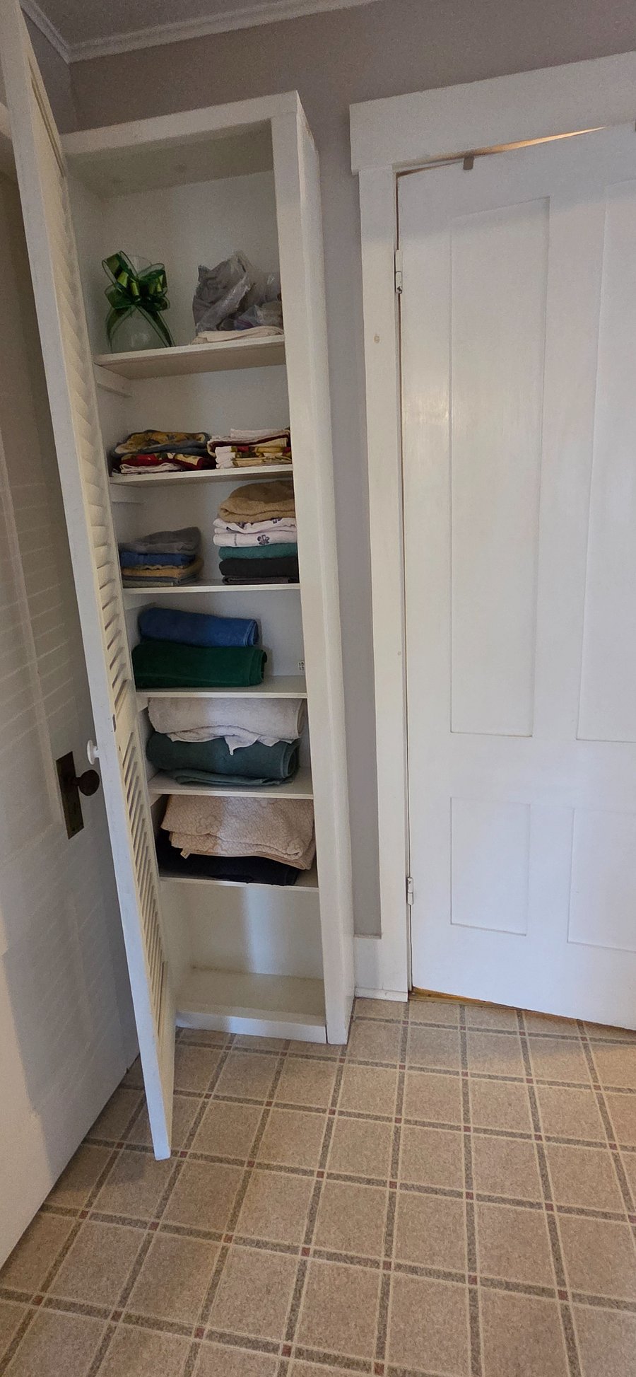 Linen closet with bath towels, hand towels, washclothes, beach towels, dish towels, hot pads and a vase. Door to the bathroom.