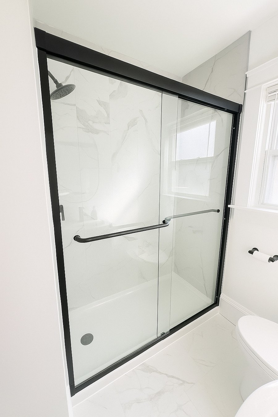 Walk-in shower with sleek black-framed glass doors and premium Moen fixtures.
