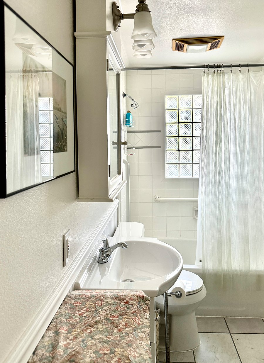 The full bathroom features a bath/shower combo, a new vanity, a new toilet, a vintage cabinet, and a glass brick window.