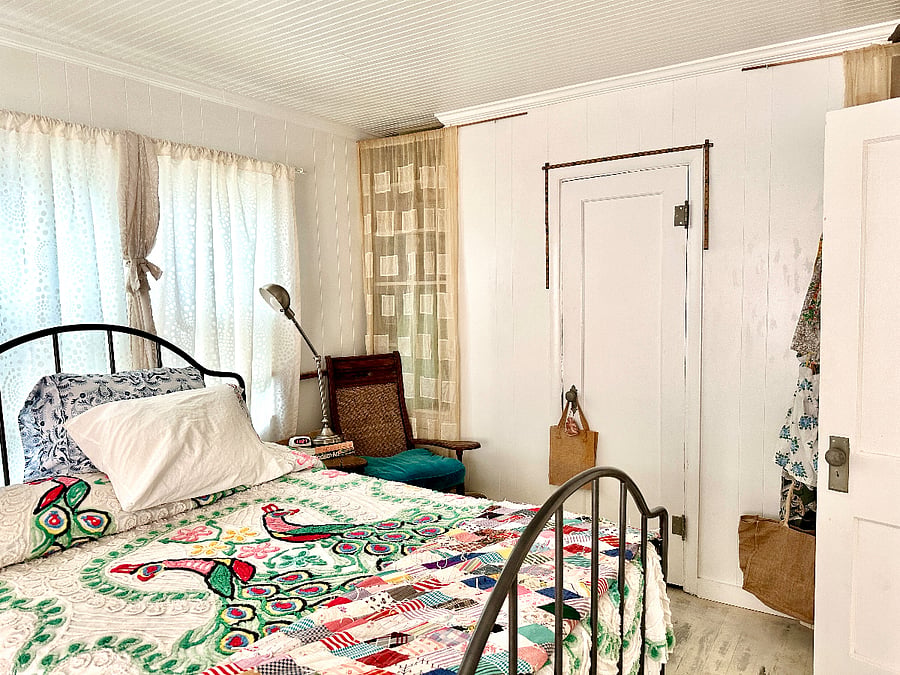 Vintage double bed with antique library chair as a bedside table with an adjustable reading lamp. All of the bedroom windows have shade rollers with various curtains: soft liners, regular, and blackout options. 
