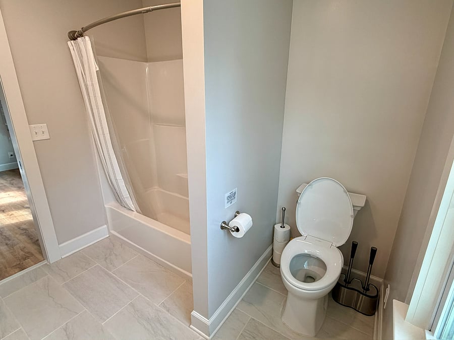 Newly renovated bathroom featuring toilet area with spare rolls and cleaning supplies.