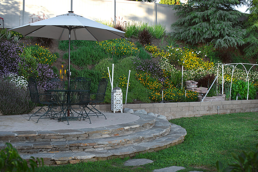 Table and chairs on the raised patio area next to the flowered hill slope 