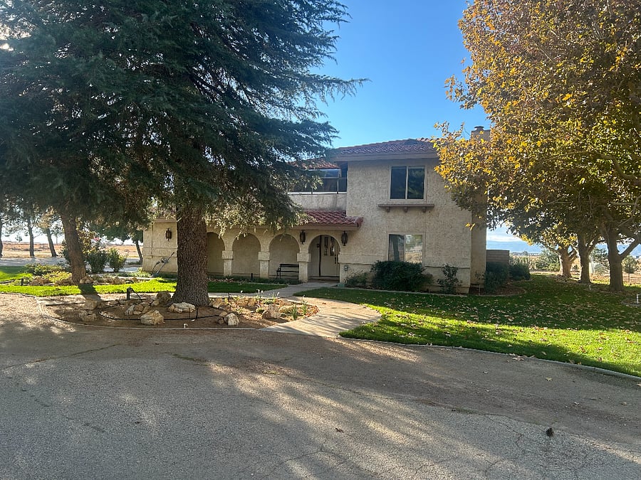Front entrance to the beautiful Spanish style home surrounded by trees, grass, and flowers