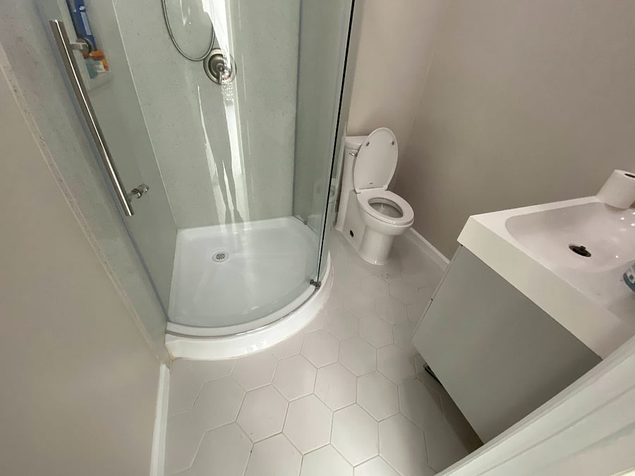 Bathroom located in hallway between two bedrooms, shower/toilet/sink