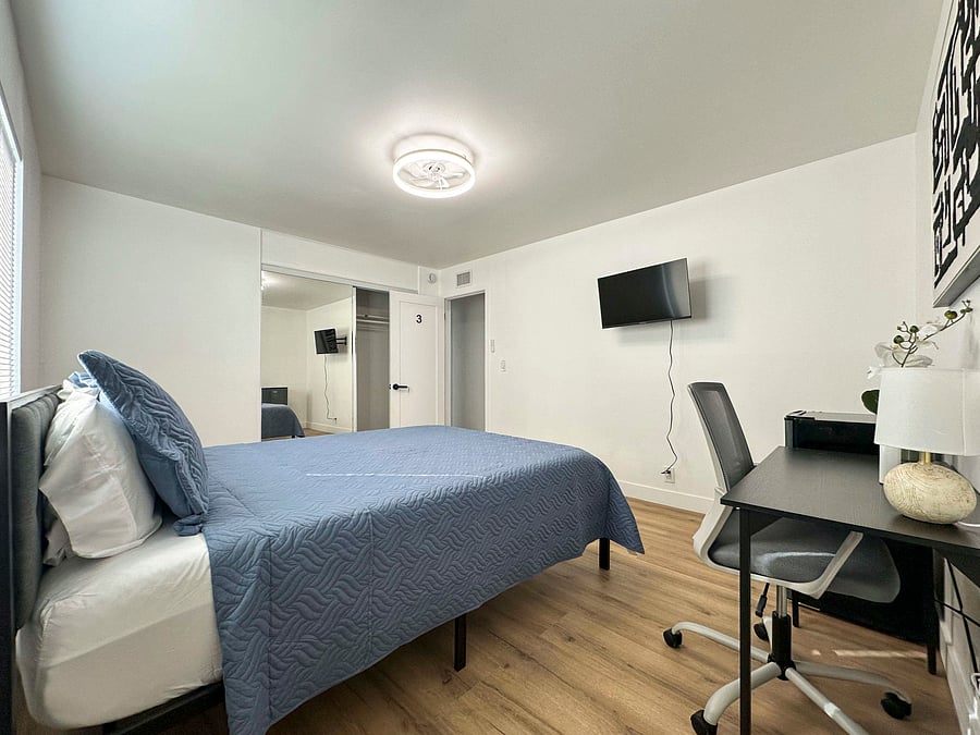 Sunny room with queen bed, desk, mini-fridge, and mirrored closet doors.