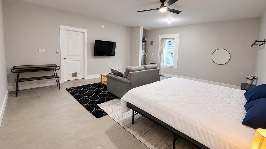 Spacious studio-style bedroom with ceiling fan, wall-mounted TV, seating area, and a window for natural light.
