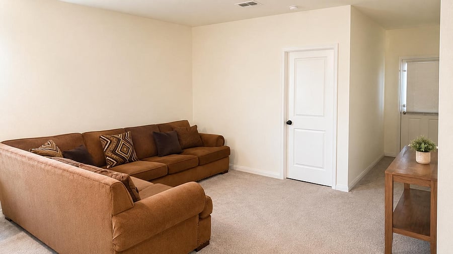 Spacious living room with a sectional seating area, neutral walls, soft carpeting, and easy access to the entry/hallway.