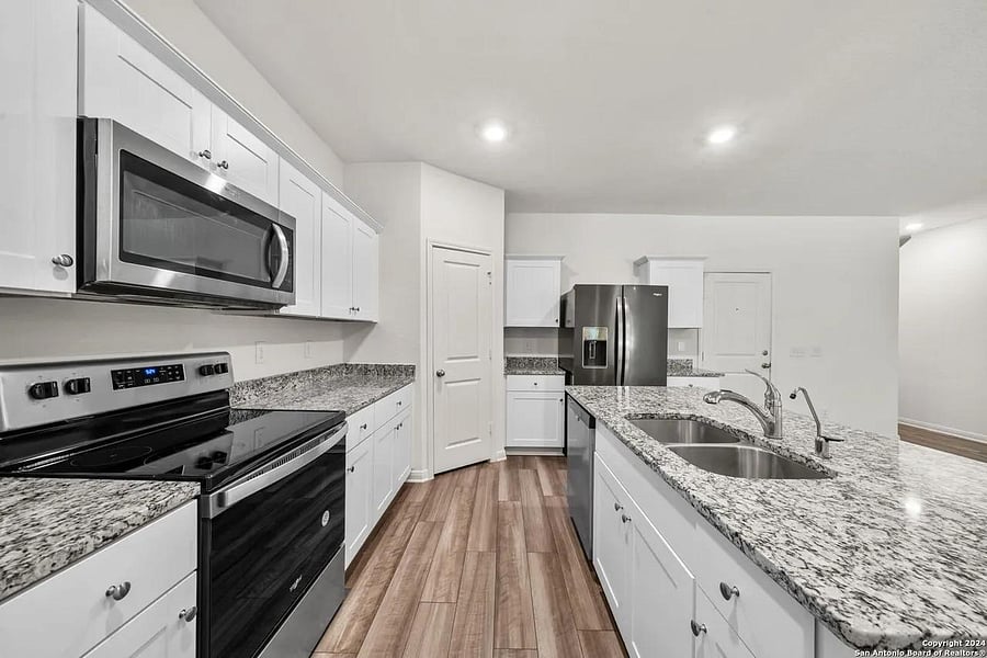 Spacious kitchen with granite counters, ample white cabinetry, stainless appliances, and a large island with double sink.