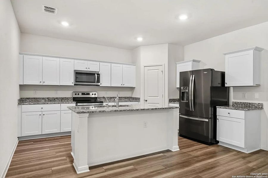 Open kitchen with granite counters, breakfast bar seating, ample white cabinetry, and stainless steel appliances.