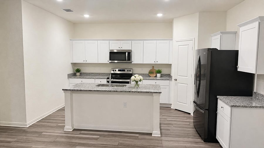 Open kitchen with large prep island, ample white cabinetry, stone-look counters, and stainless appliances plus pantry.