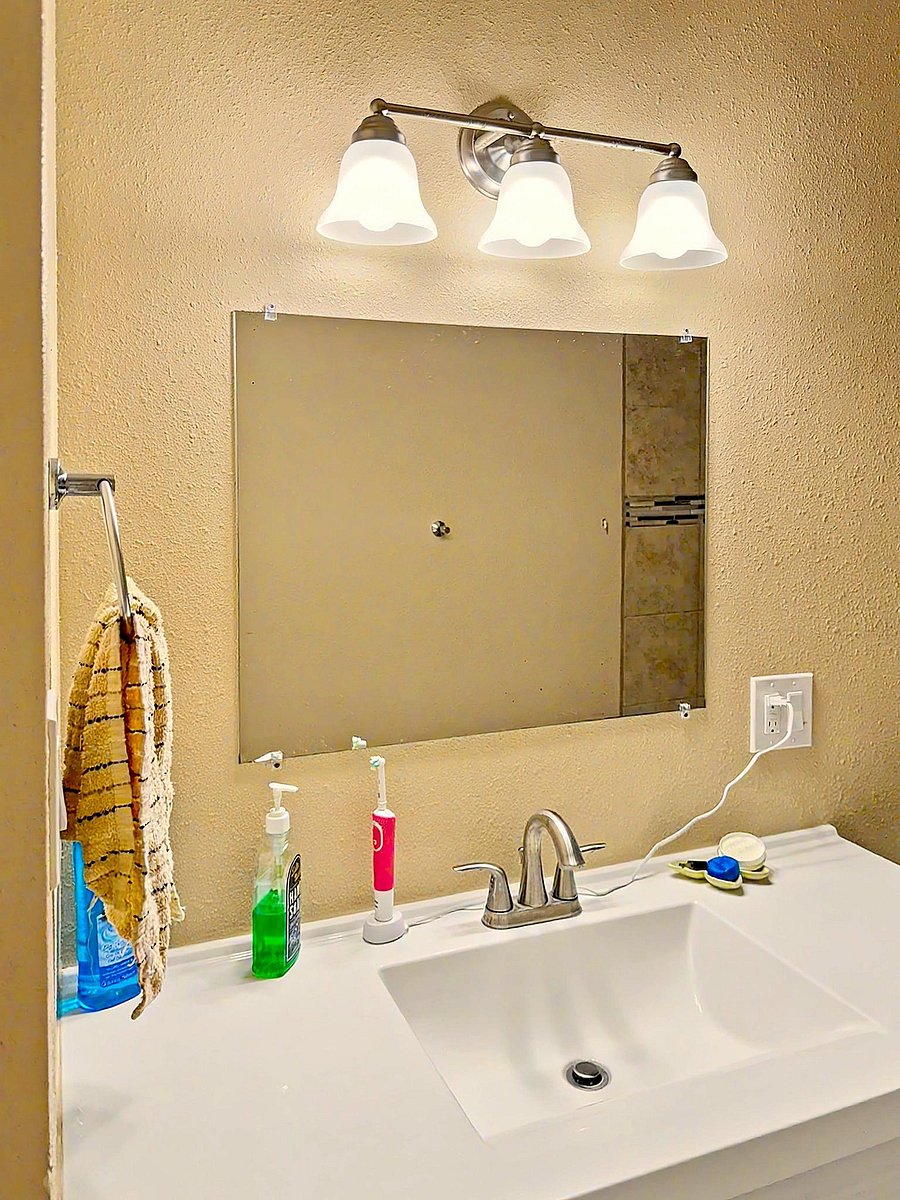 Bathroom vanity area featuring a wide mirror, overhead three-light fixture, and a clean white sink with chrome faucet.