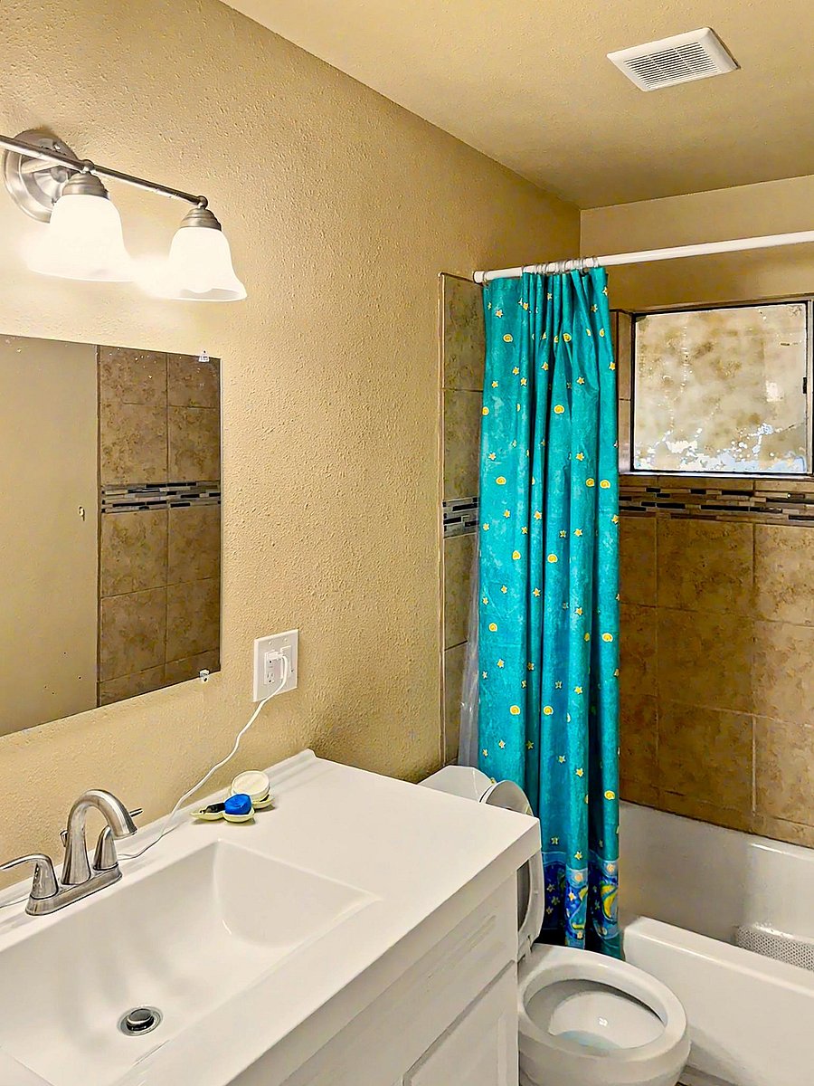 Full bathroom with vanity storage, wall mirror, and a shower/tub combo with tiled surround and window for ventilation.