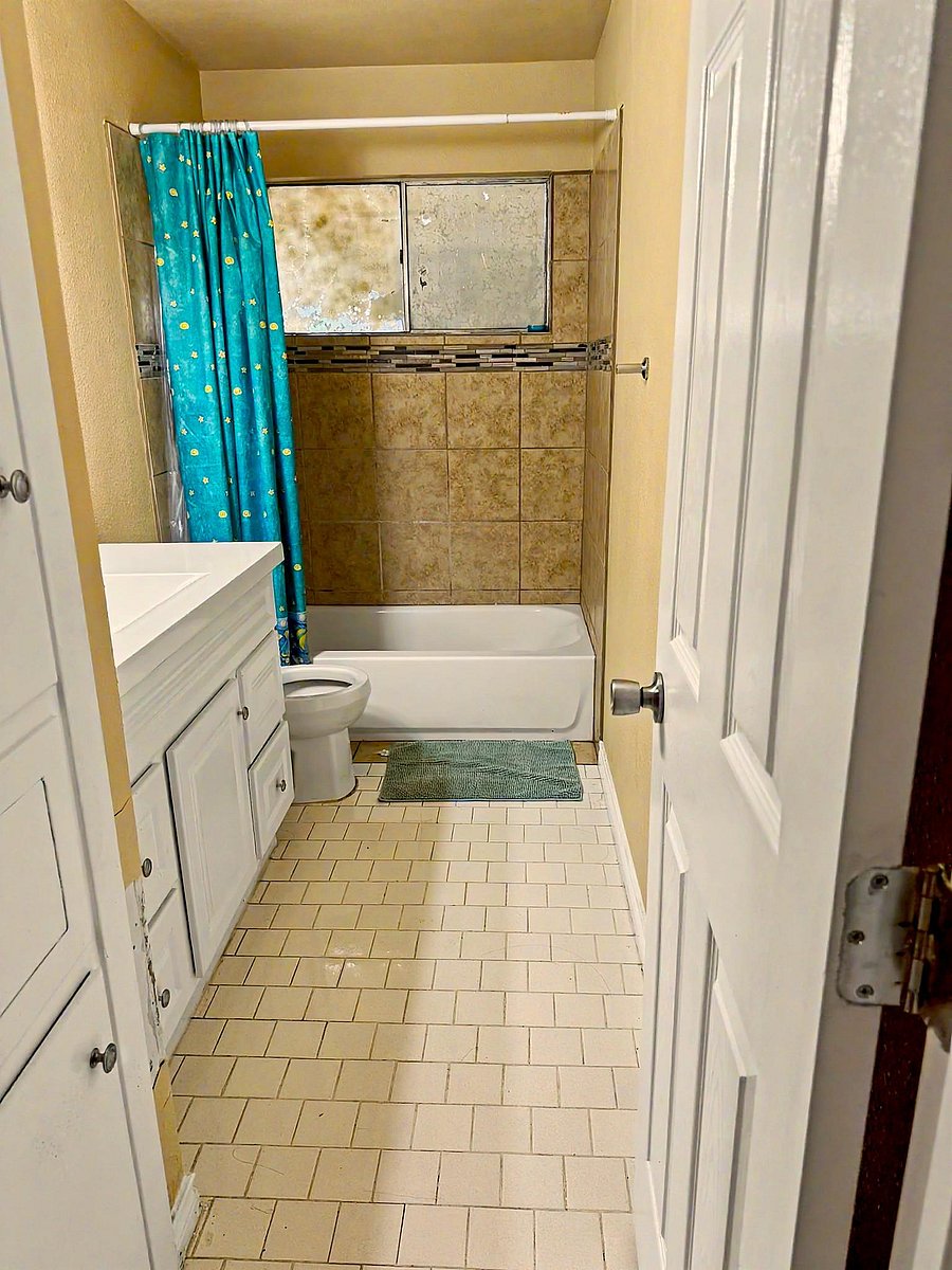 Full bathroom with tiled tub/shower surround, vanity storage, and a shower curtain for added privacy.