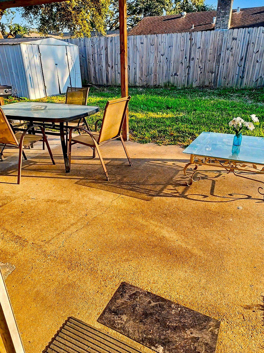 Covered backyard patio with outdoor table seating, open lawn space, and a storage shed--ideal for relaxing or entertaining.