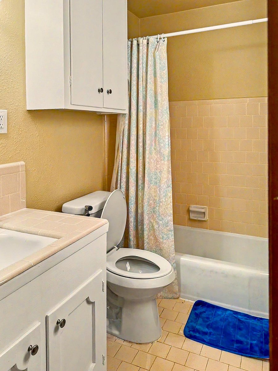 Full bathroom with tub/shower combo, tiled surround, and vanity storage plus an over-toilet cabinet for essentials.