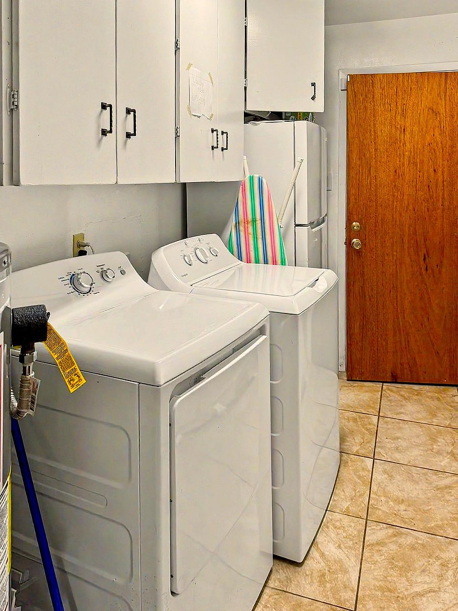 Dedicated laundry area with full-size washer and dryer, overhead storage cabinets, and durable tile flooring.