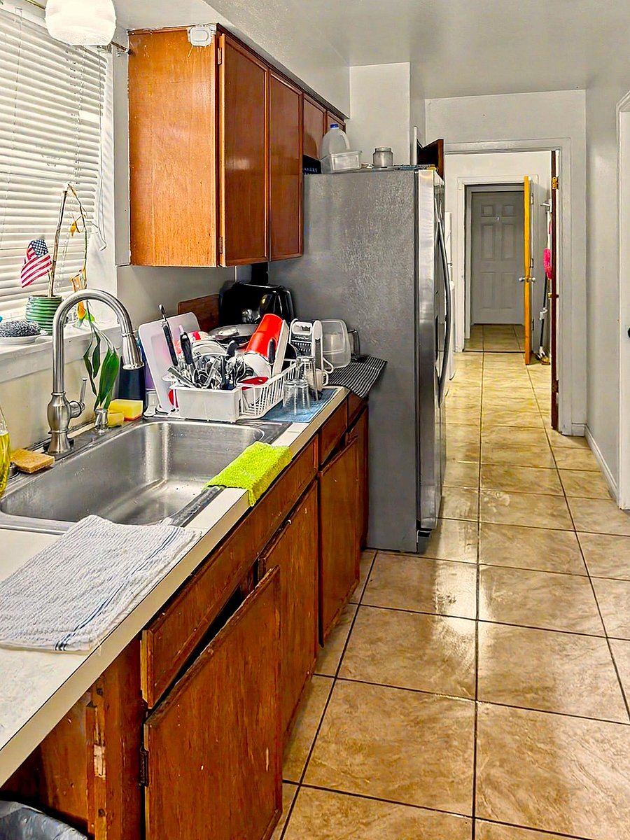 Galley-style kitchen with ample wood cabinetry, full-size refrigerator, and a double-basin sink beside a window.
