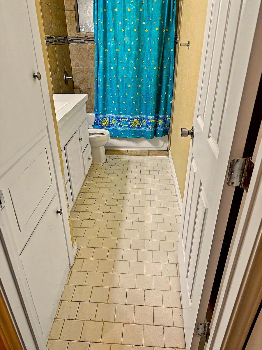 Full bathroom with a tub/shower combo, tiled surround, vanity storage, and a window for ventilation and natural light.