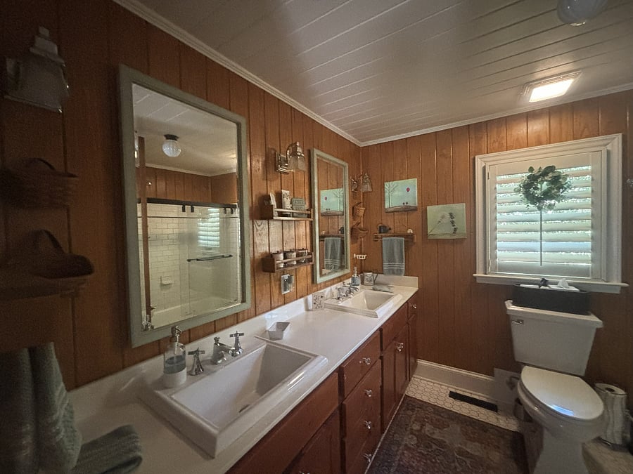 The large bathroom features double sinks, lots of storage, and a tub with glass shower doors.