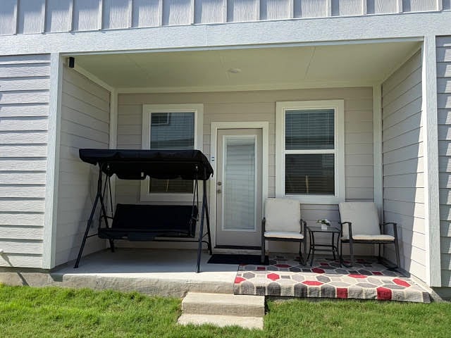 Private side covered patio with chairs, a swing, side table, and a floor mat.
