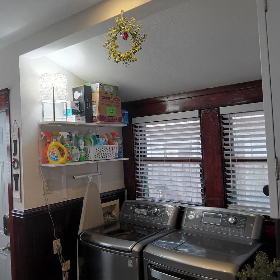 Laundry space in kitchen with wrap-around windows and shelves for supplies.