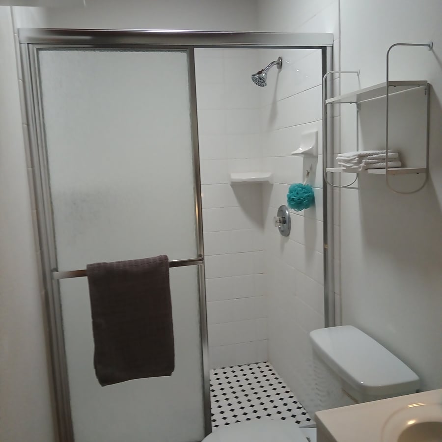 Shower stall has sliding raindrop glass doors, one with a towel bar.