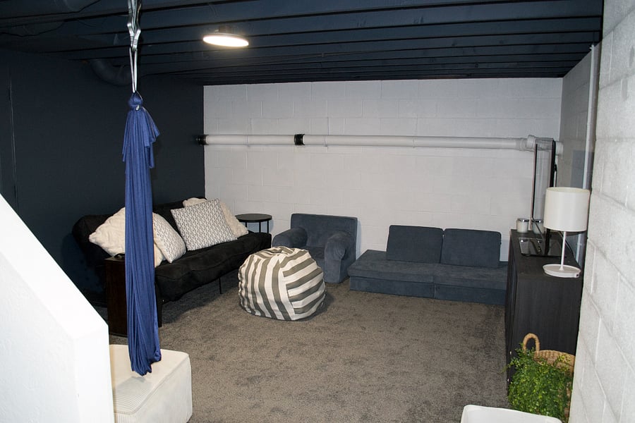 The finished lower level is divided into two functional spaces. One side (pictured) is a rec room with a futon couch, chair & ottoman, plenty of comfortable stuffed items, and a TV w/ Roku. There's also sensory swings attached to the ceiling.