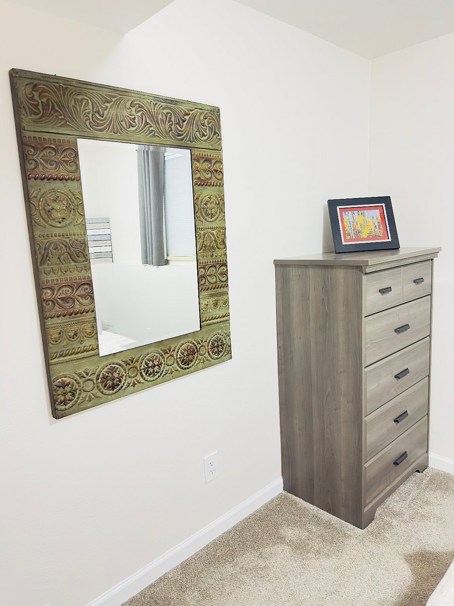 Bedroom 2 includes a spacious dresser for storage and a large decorative mirror, offering a functional and comfortable setup with a clean, uncluttered feel.