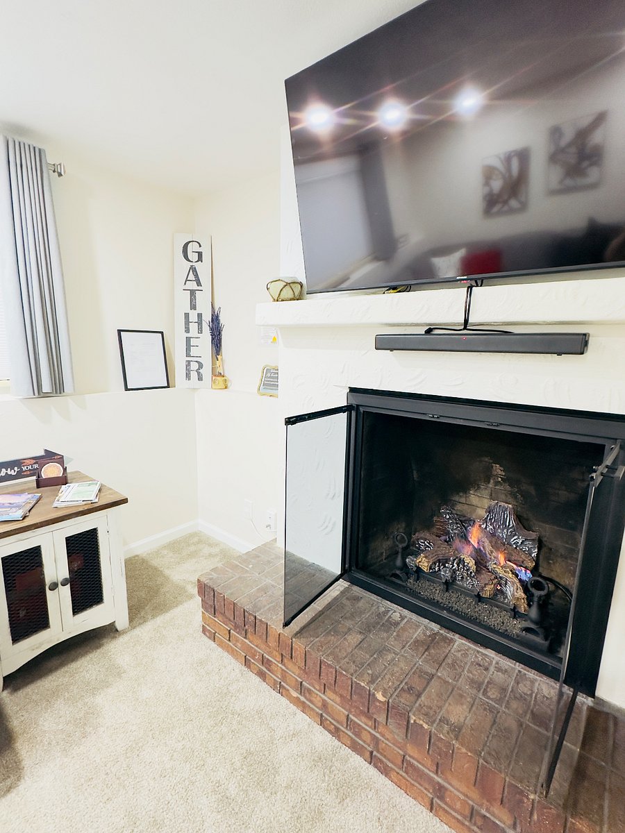 Cozy living room featuring a warm gas fireplace with a brick hearth, mounted TV above the mantel, and soft lighting. A comfortable, inviting space perfect for relaxing after a day of exploring.