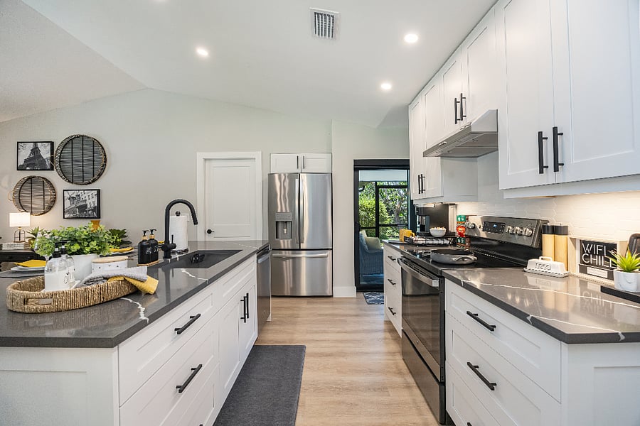 Bright, fully renovated kitchen with white shaker cabinets, quartz countertops, and stainless steel appliances. Sliding door opens to the covered lanai.