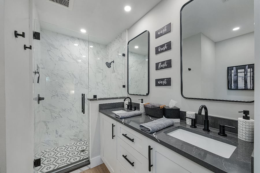 Double vanity with quartz counters and black fixtures, plus a glass walk in shower with decorative tile. Fresh towels and starter toiletries provided.
