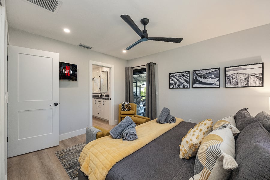 King bedroom with a wall-mounted smart TV and direct access to the ensuite bath. Glass door opens to the patio for fresh morning air.