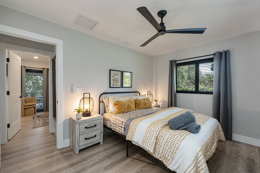 Queen bed with cozy bedding, nightstands with lamps, and a quiet ceiling fan. Window shades help keep the room dark for restful sleep.