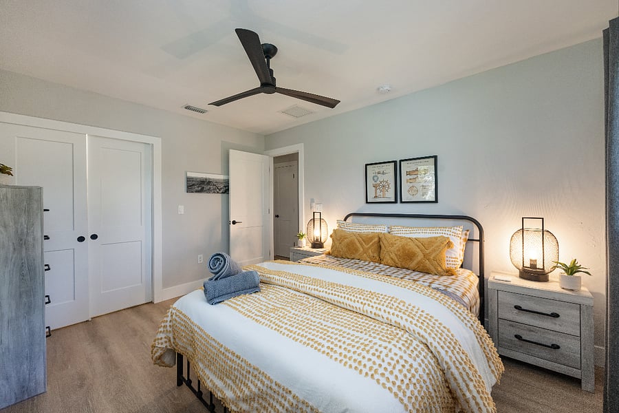 Queen bedroom with sliding closet doors and a dresser for easy storage. Soft lighting and fresh towels ready on the bed.