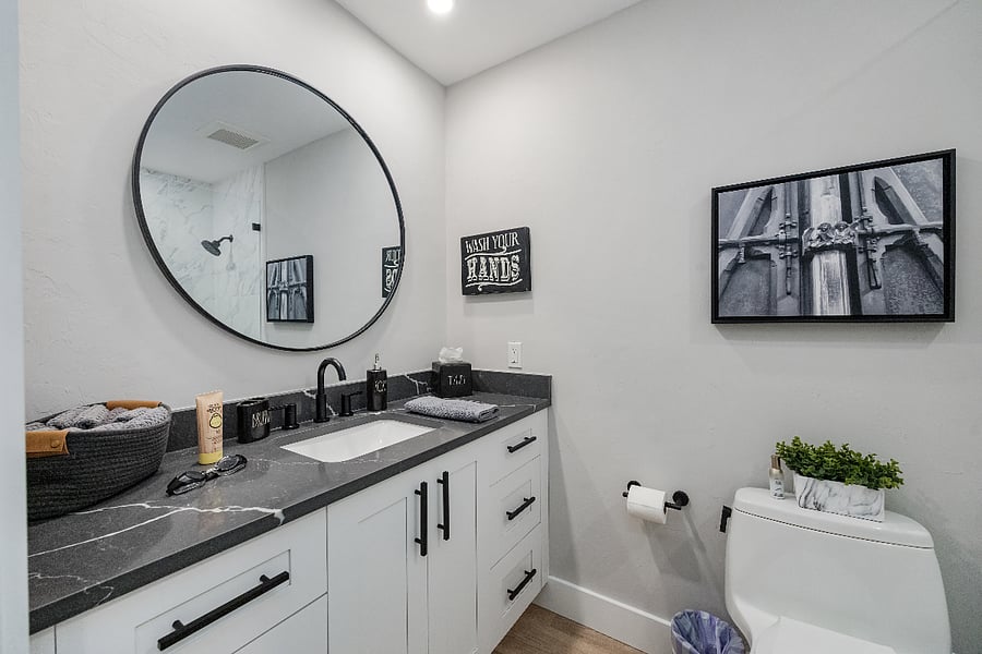 Quartz vanity with round mirror and black fixtures. Fresh towels and starter toiletries provided.