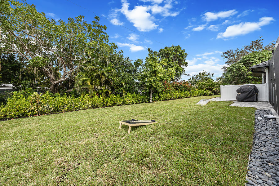 Kick back in the private yard featuring lush landscaping, a gas grill for outdoor cooking, and a corn hole setup for some friendly competition under the sun.