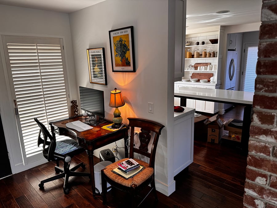 Graphics workstation: color enhanced monitor, ergonomic keyboard, sturdy office chair, and antique desk. Discrete brick and garden view with natural light through adjustable blinds.