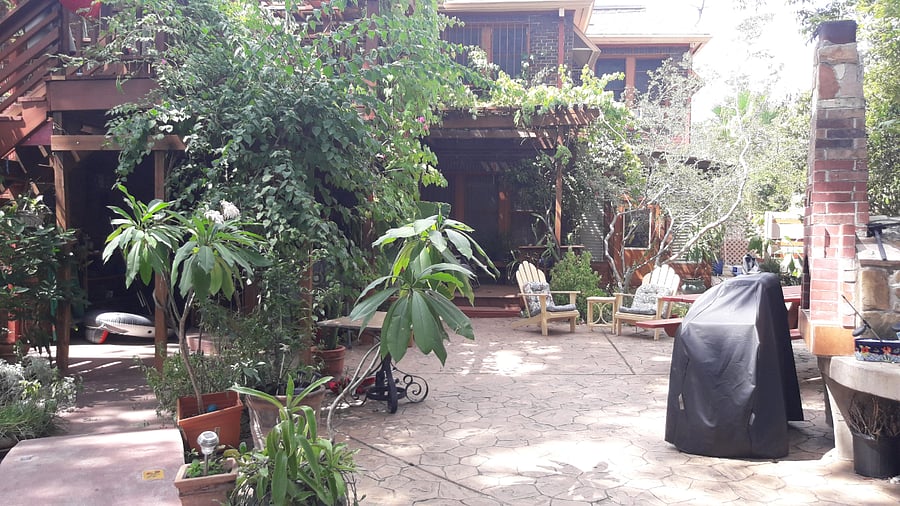 Large fenced yard below deck with grill, pizza oven, & gardens