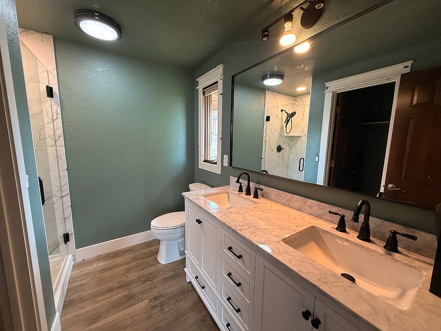 Newly remodeled bathroom features double vanity/sink, new lighting, toilet, shower.
