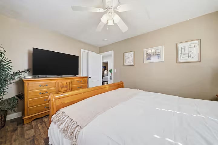 Cozy bedroom retreat with a plush bed, ceiling fan, and TV for added comfort. Warm wood furniture and tasteful wall art create a welcoming space to relax and recharge.