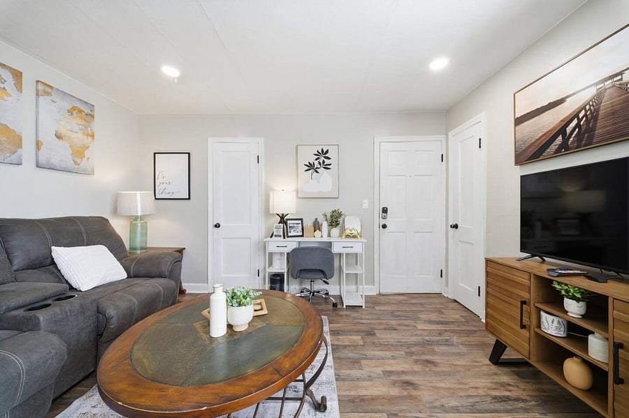 Relax in this stylish living space featuring a smart TV, comfortable seating, and a dedicated workspace. Clean lines, modern artwork, and warm wood floors create a cozy yet functional area for both leisure and productivity.