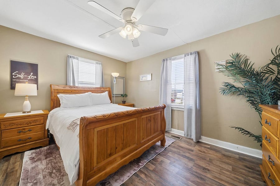 Inviting bedroom with a beautiful wooden bed frame, soft linens, and warm lighting. A ceiling fan and natural light create a comfortable, restful space to unwind at the end of the day