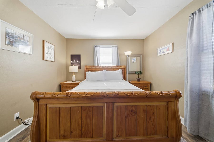 Relaxing bedroom with a sturdy wooden bed, soft bedding, and warm bedside lighting. Thoughtful dcor and natural light create a peaceful setting for a restful nights sleep.